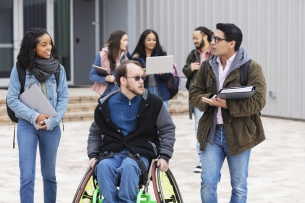 Students carrying books chat on a college campus.